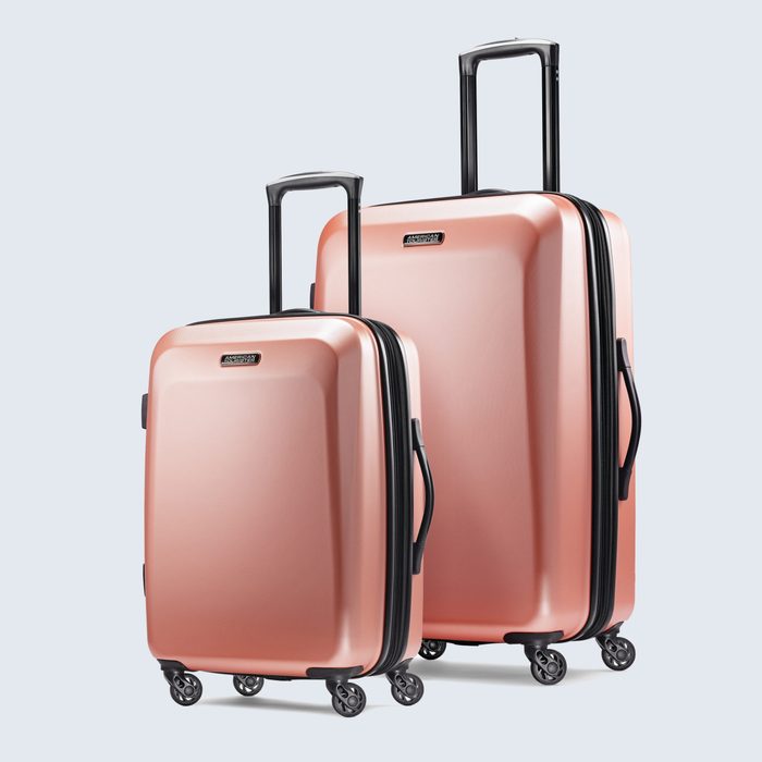 Two rose gold suitcases stand upright with extended handles; both have four wheels each, set against a plain light-colored background.