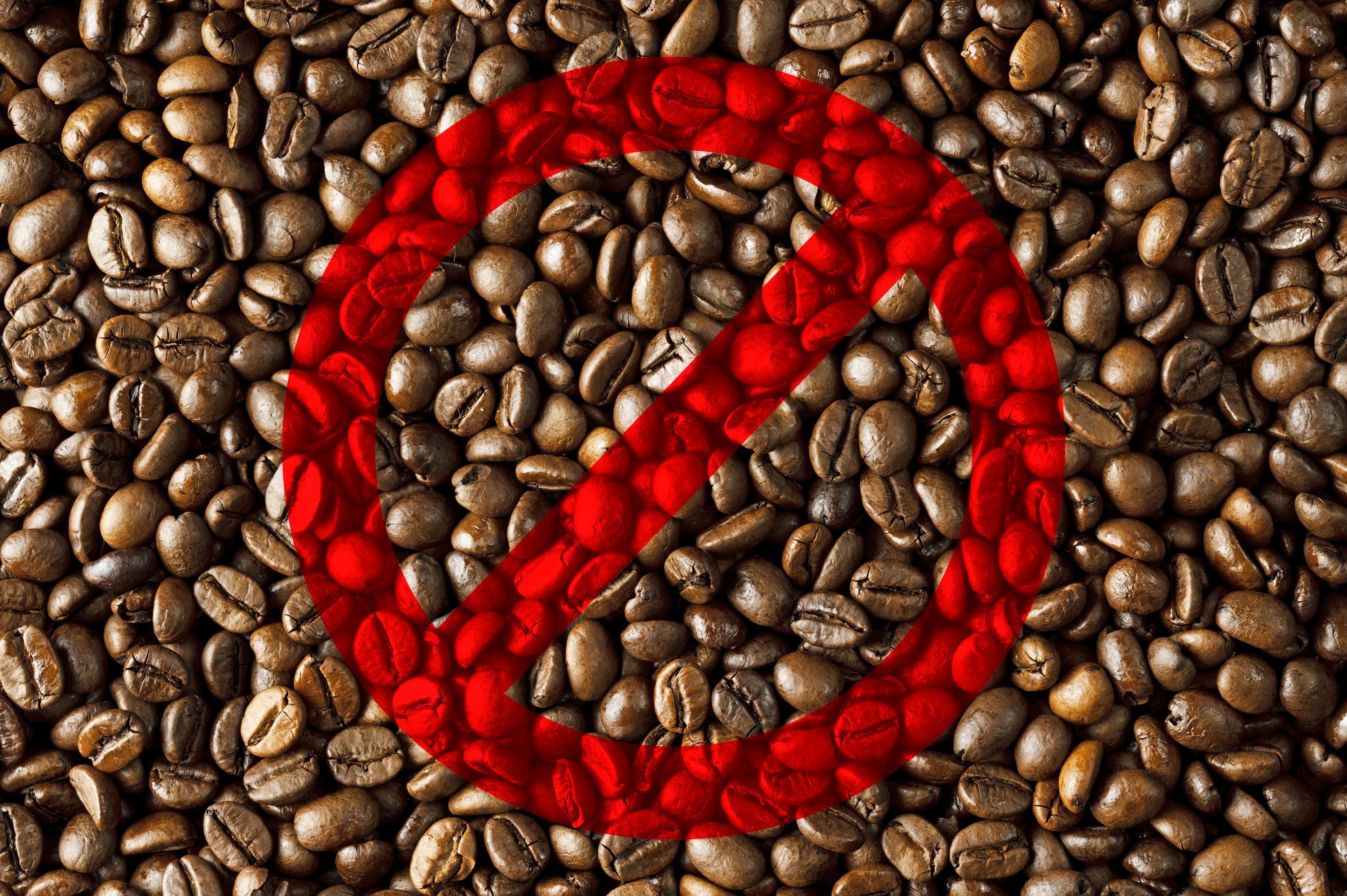 Coffee beans covered by a large red prohibition symbol, indicating a restriction or ban, in a textured background.
