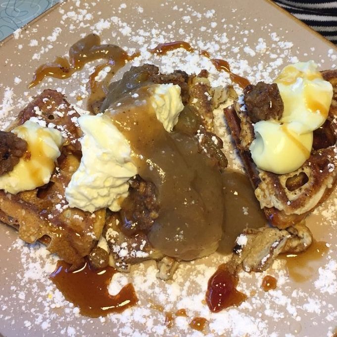Waffles topped with whipped cream, gravy, and powdered sugar sit on a plate, surrounded by drizzled syrup.