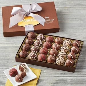 Box of assorted chocolates displayed on wooden table; some chocolates on small white plate. Box is labeled 