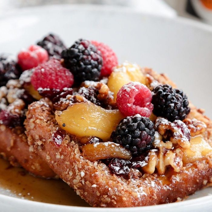 French toast topped with blackberries, raspberries, and walnuts, drizzled with syrup, on a white plate.