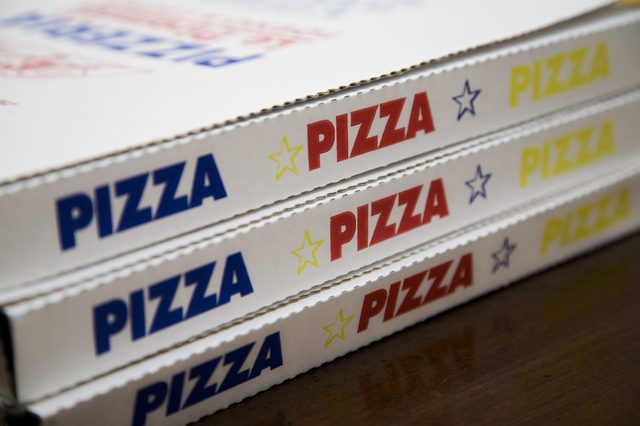 Boxes stacked, displaying "PIZZA" in red, yellow, blue with stars, on a wooden surface.
