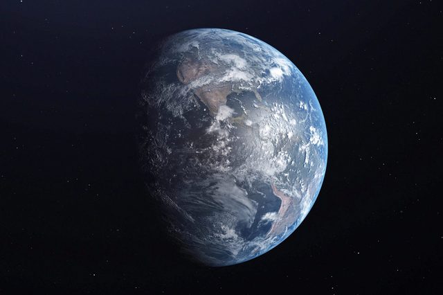 Earth partially illuminated, displaying continents and clouds, floating in dark space scattered with distant stars.
