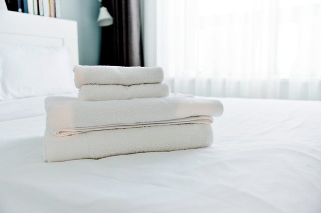 Towels are stacked neatly on a bed, illuminated by soft natural light from a nearby window.