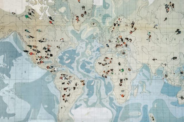Illustrated world map showing figures engaged in various activities, scattered across continents, with muted blue and beige color tones.