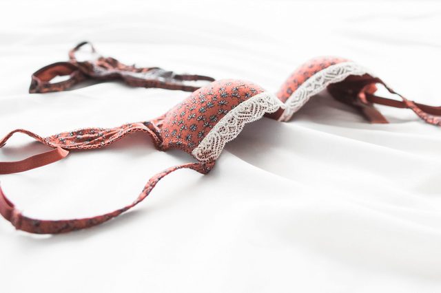 A floral-patterned bra with lace trim lies on a smooth white fabric, creating a serene and intimate setting.