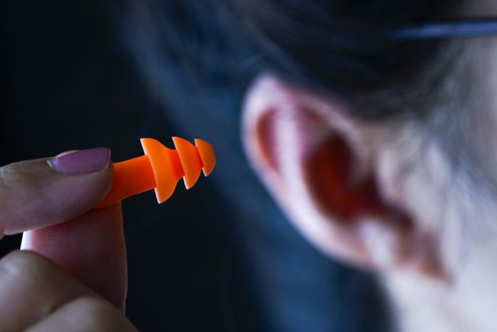 An orange earplug is being held near an ear in a dimly lit room.