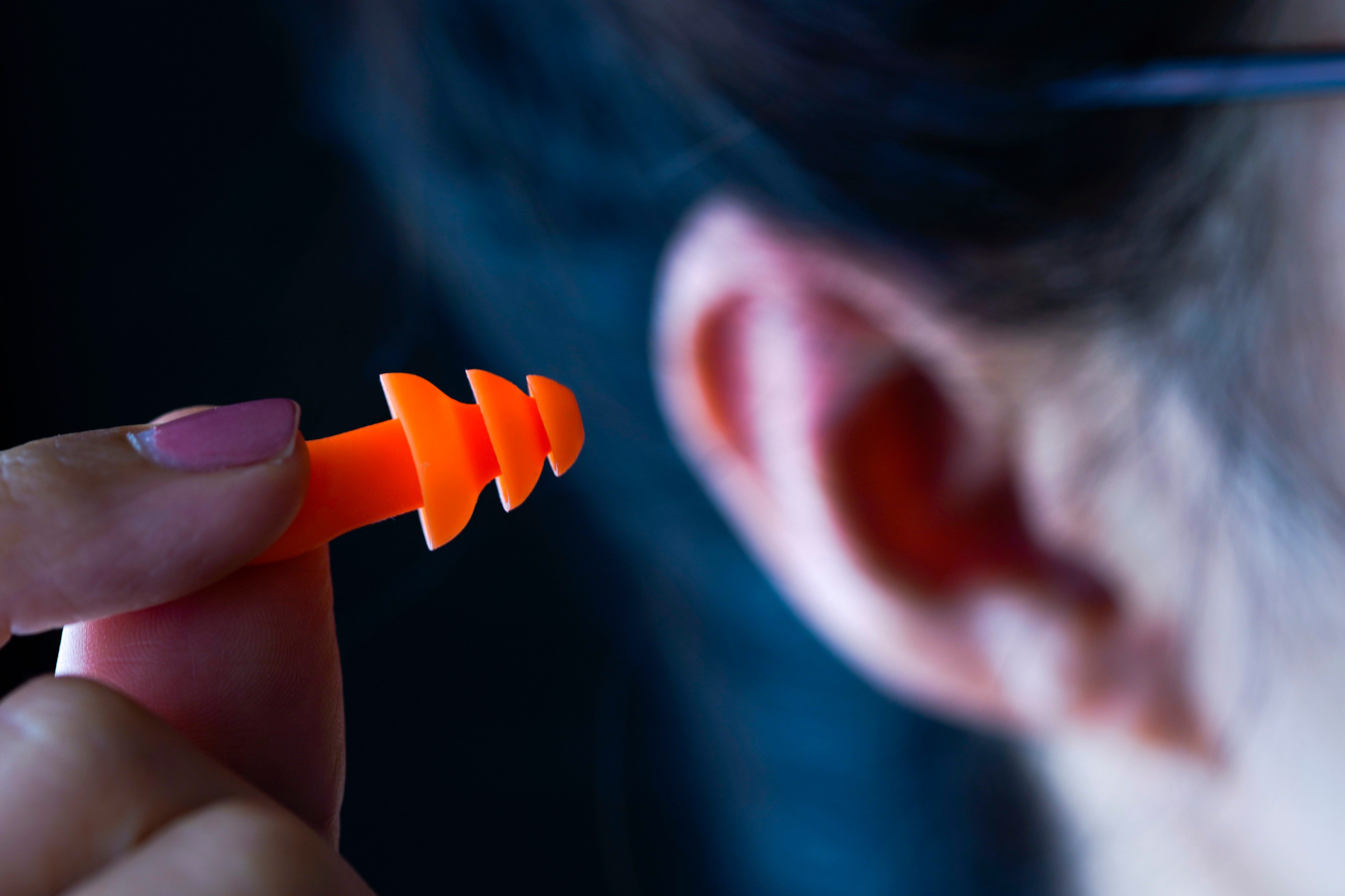An orange earplug is being held near an ear in a dimly lit room.