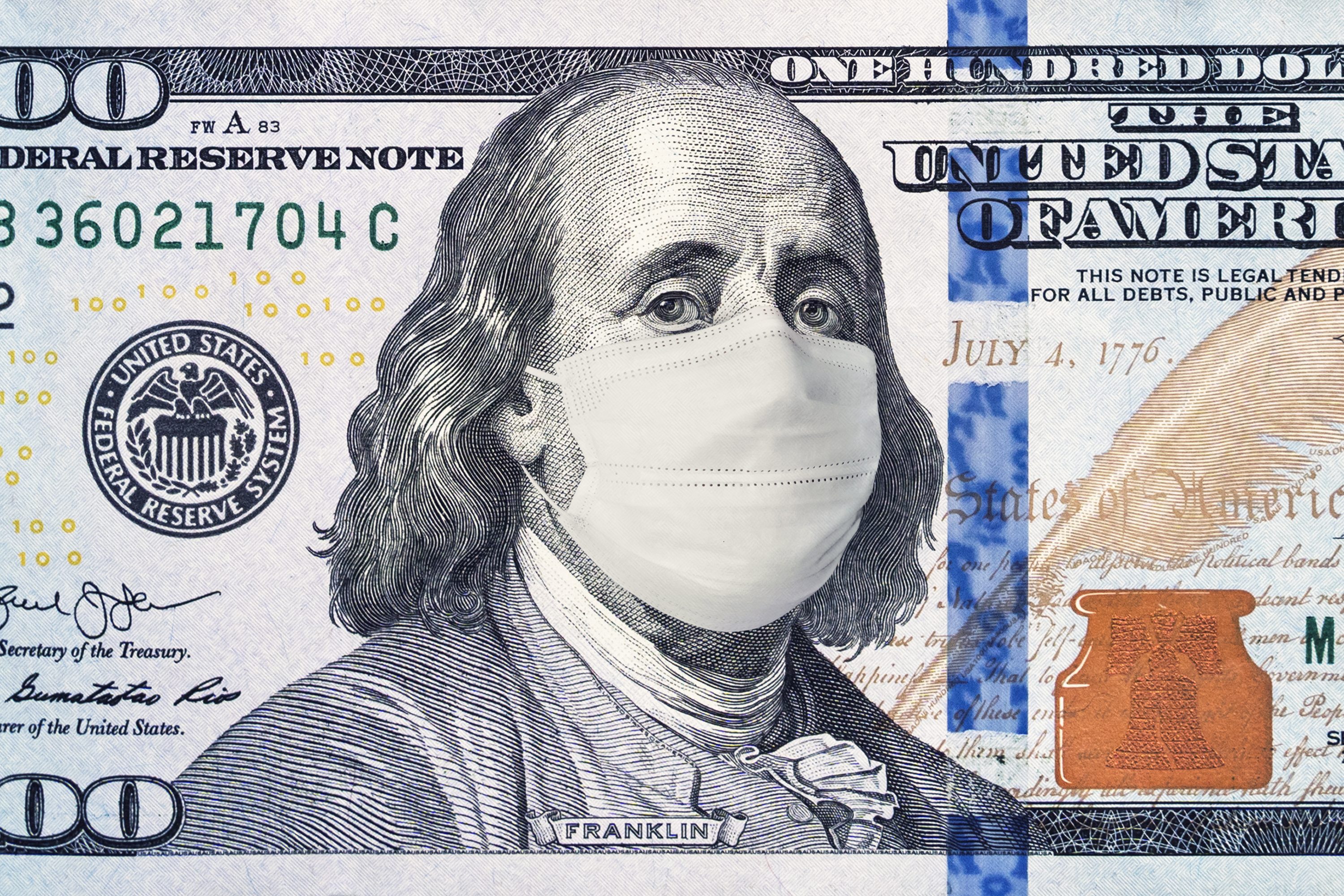 A hundred-dollar bill shows Benjamin Franklin wearing a medical mask, with intricate security features and text revealing "United States of America" and "Federal Reserve Note."