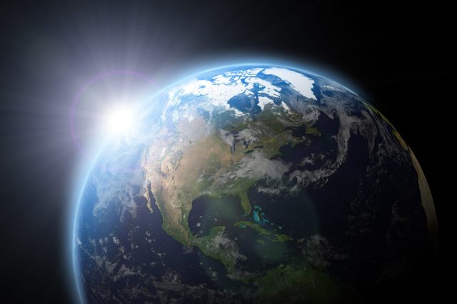 Earth partially illuminated by sunlight, seen from space, with visible continents and ocean, surrounded by darkness.