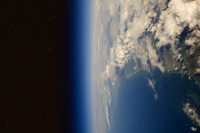 Earth is viewed from space, showing clouds and landmass curved against the vast black expanse of the universe.