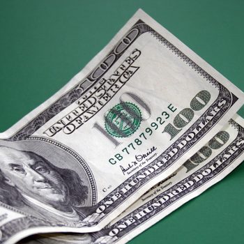 Stack of three hundred-dollar bills lying on a flat, green surface.