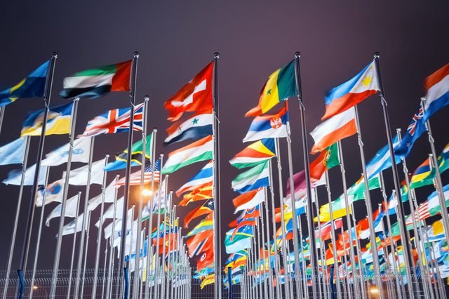 Flags wave on poles; vibrant colors fill the night sky, symbolizing diverse nations in a gathering or international event setting.