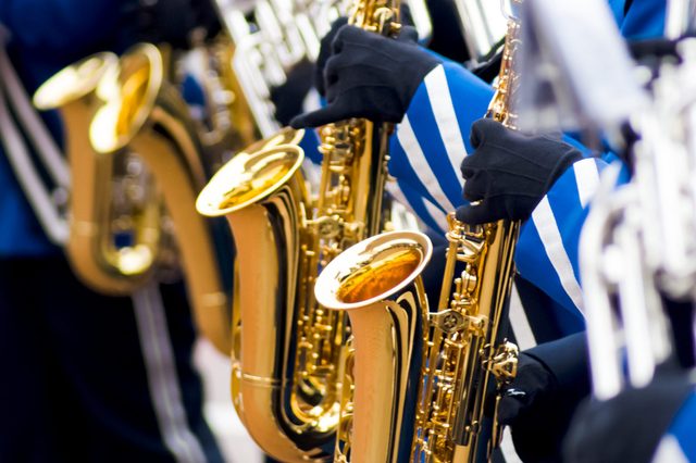 Saxophones played by musicians wearing blue and white uniforms, with gloved hands visible in a marching band setting.