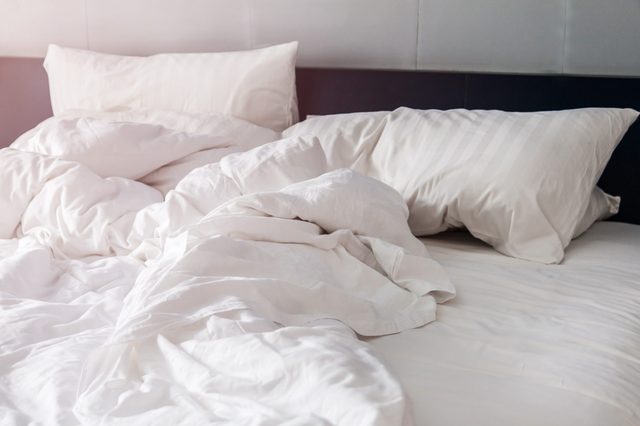 Bed with white, rumpled sheets and pillows; soft morning light filters into the room.