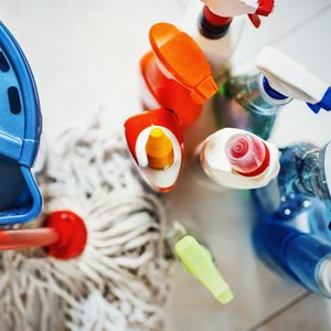 Cleaning supplies are gathered, including spray bottles, a mop, and a blue bucket on a tiled floor, ready for use.