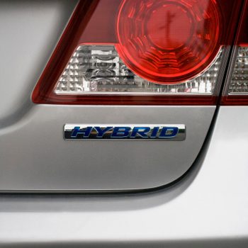 Car taillight shines, with "HYBRID" badge attached, set against a metallic grey vehicle body.