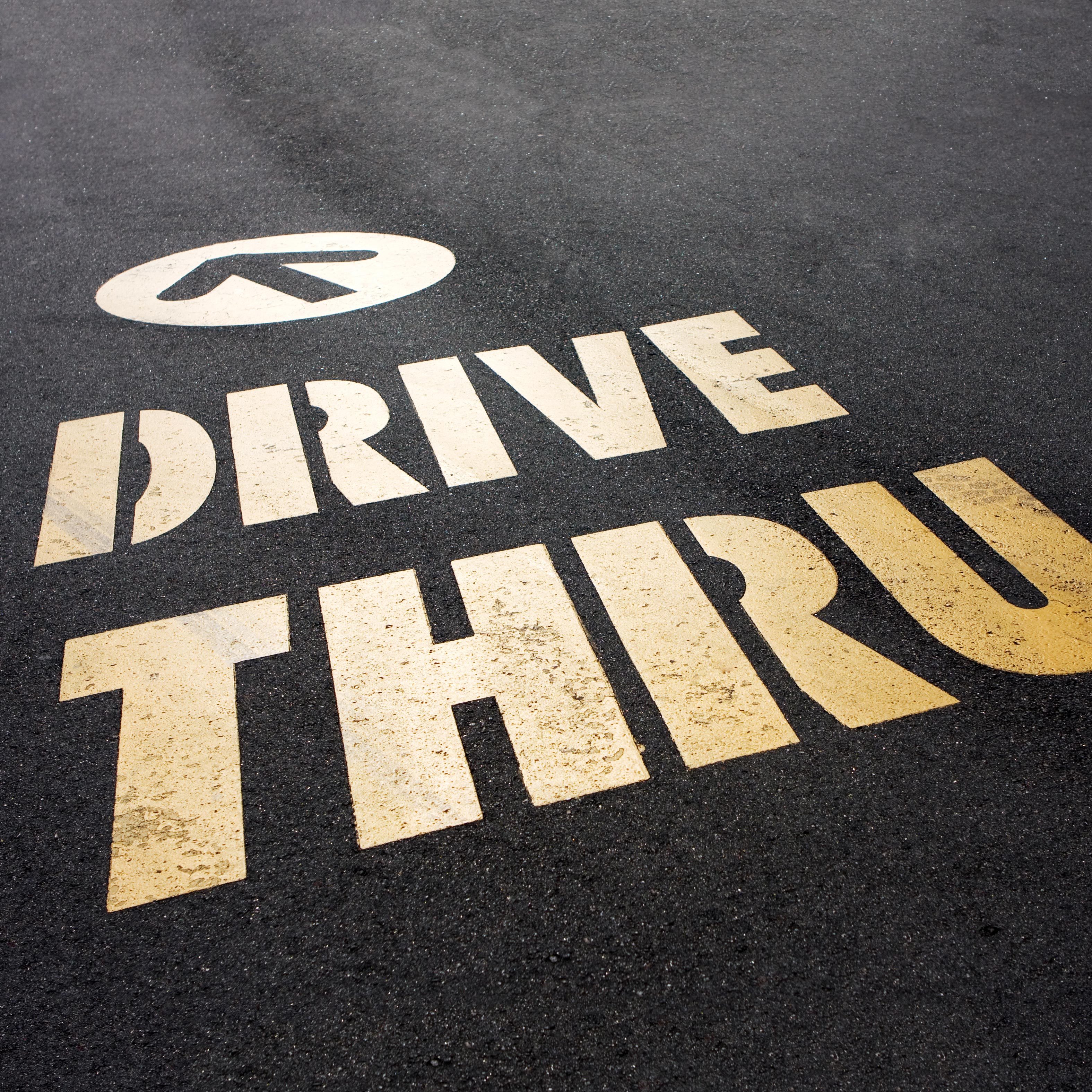 Words "DRIVE THRU" painted on asphalt with a directional arrow above, indicating the direction to proceed in a drive-through area.