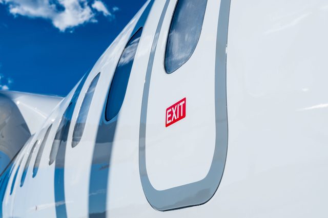 Airplane exit door with red "EXIT" sign, under clear blue sky and white clouds.