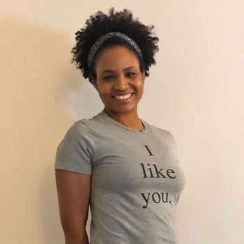 A person smiles while standing; wearing a grey T-shirt with the text "I like you," against a plain background.