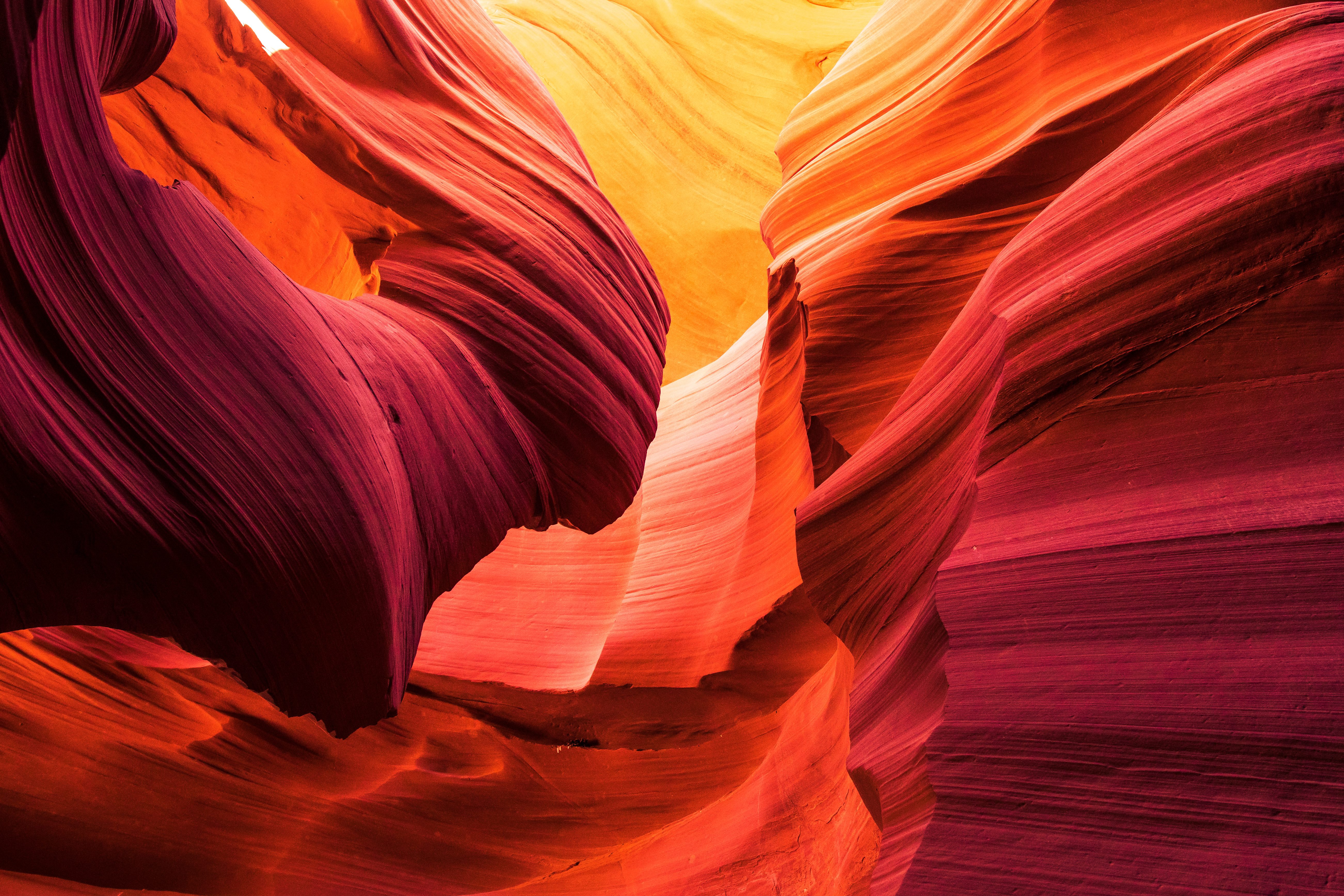 Sunlight illuminates smooth, flowing rock formations. The vibrant orange and red hues reflect canyon walls in a winding, narrow passage.