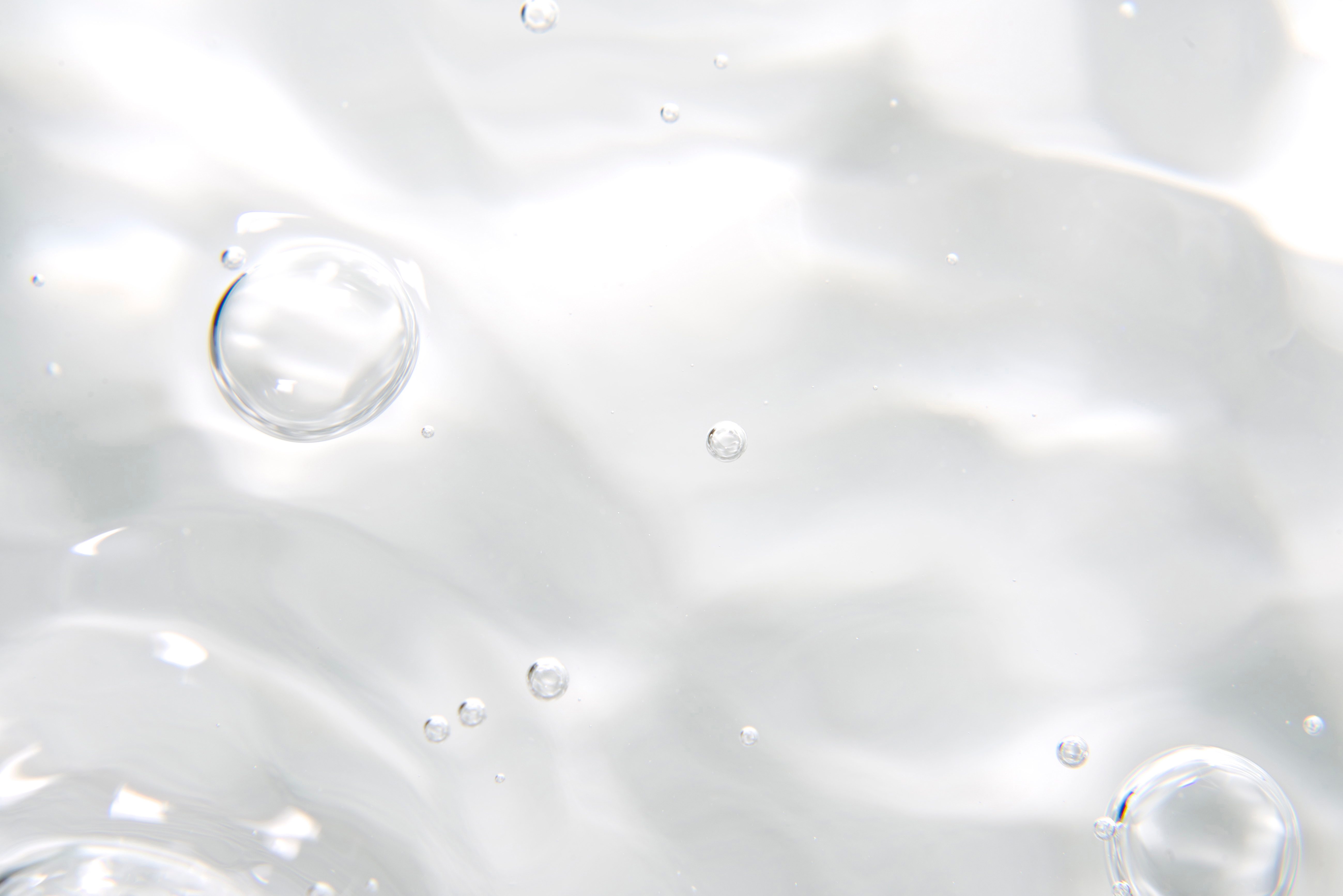 Bubbles float through clear liquid, creating shimmering ripples against a soft, blurred background.