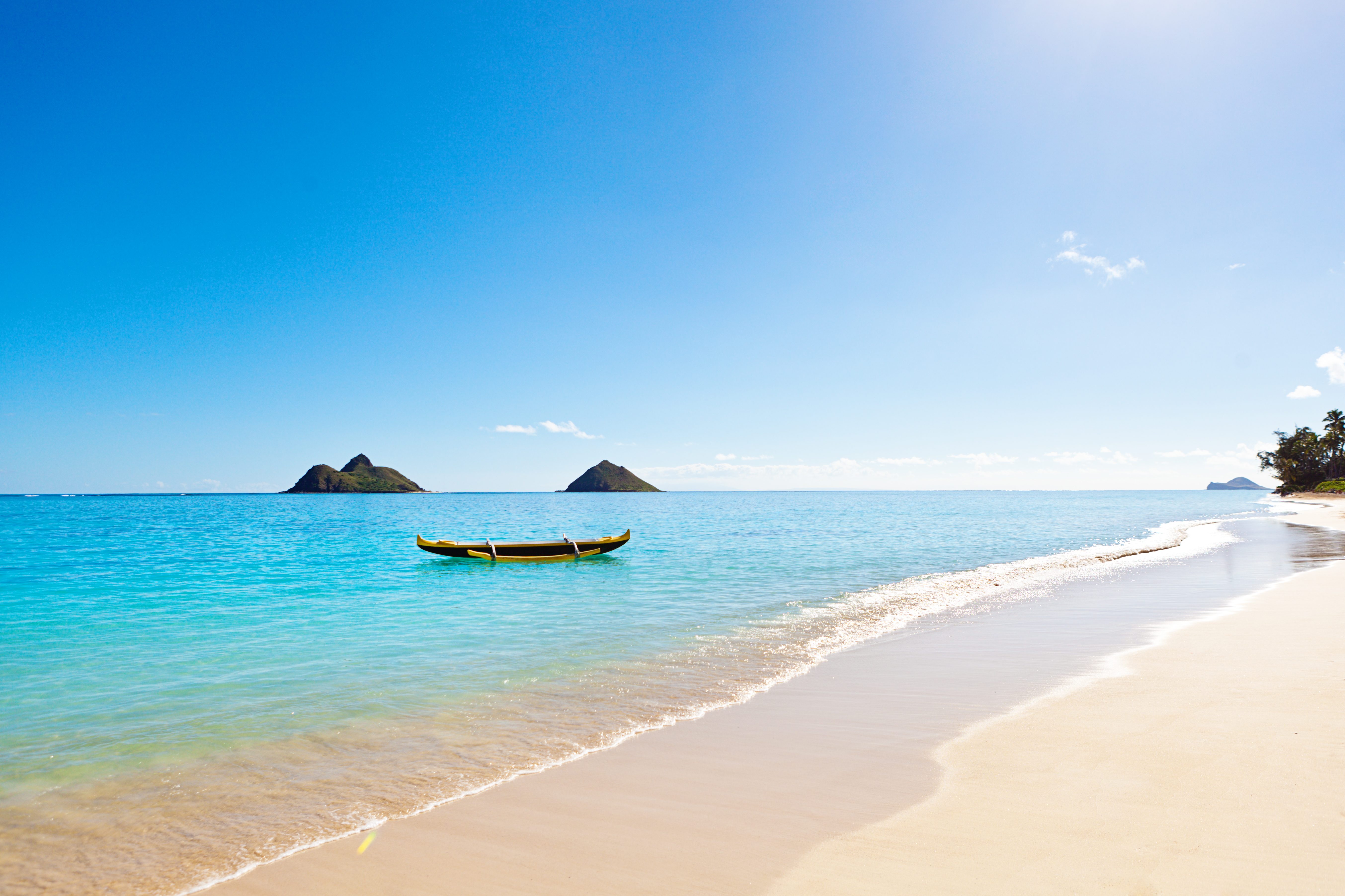 Canoe floats on calm turquoise sea, near sandy beach with distant islands under clear blue sky.