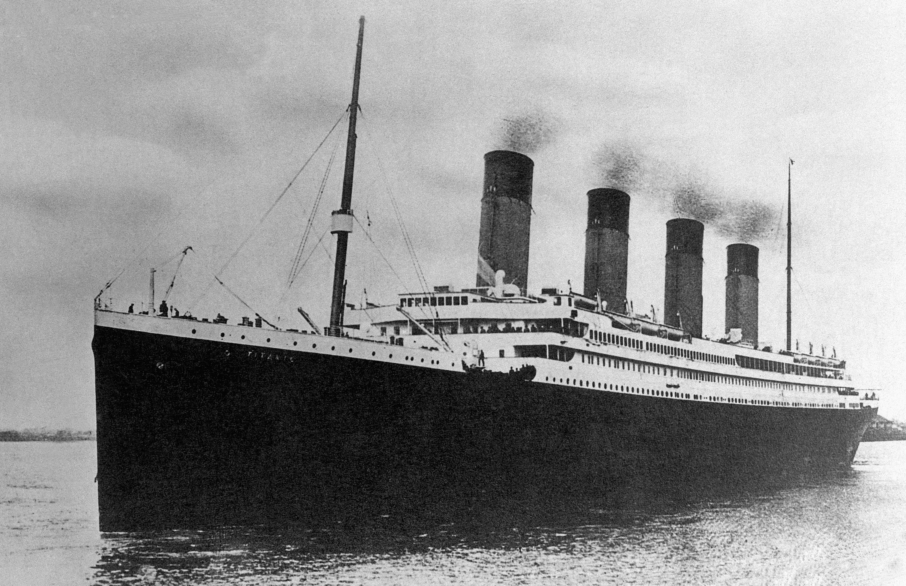 A large ship with four smokestacks sails on calm water, surrounded by open sea and cloudy sky; text reads "TITANIC" on the hull.