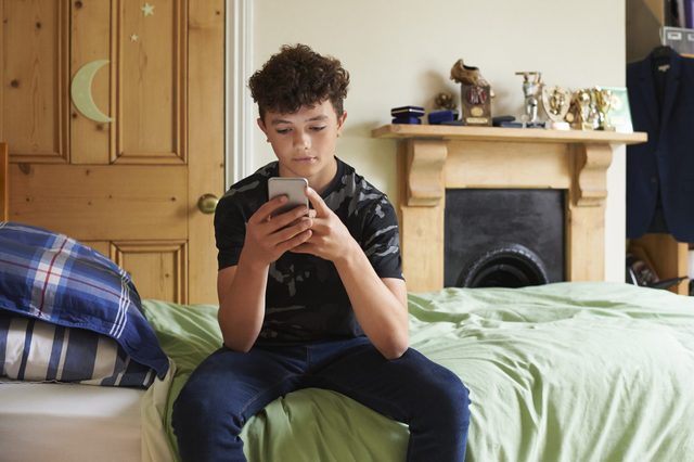 Teenage boy in his bedroom texting on smartphone
