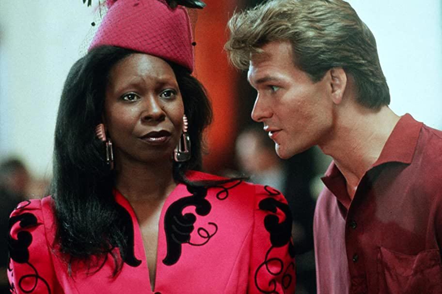 Woman wearing a pink outfit listens intently, while a man in a red shirt speaks to her in a crowded indoor setting.
