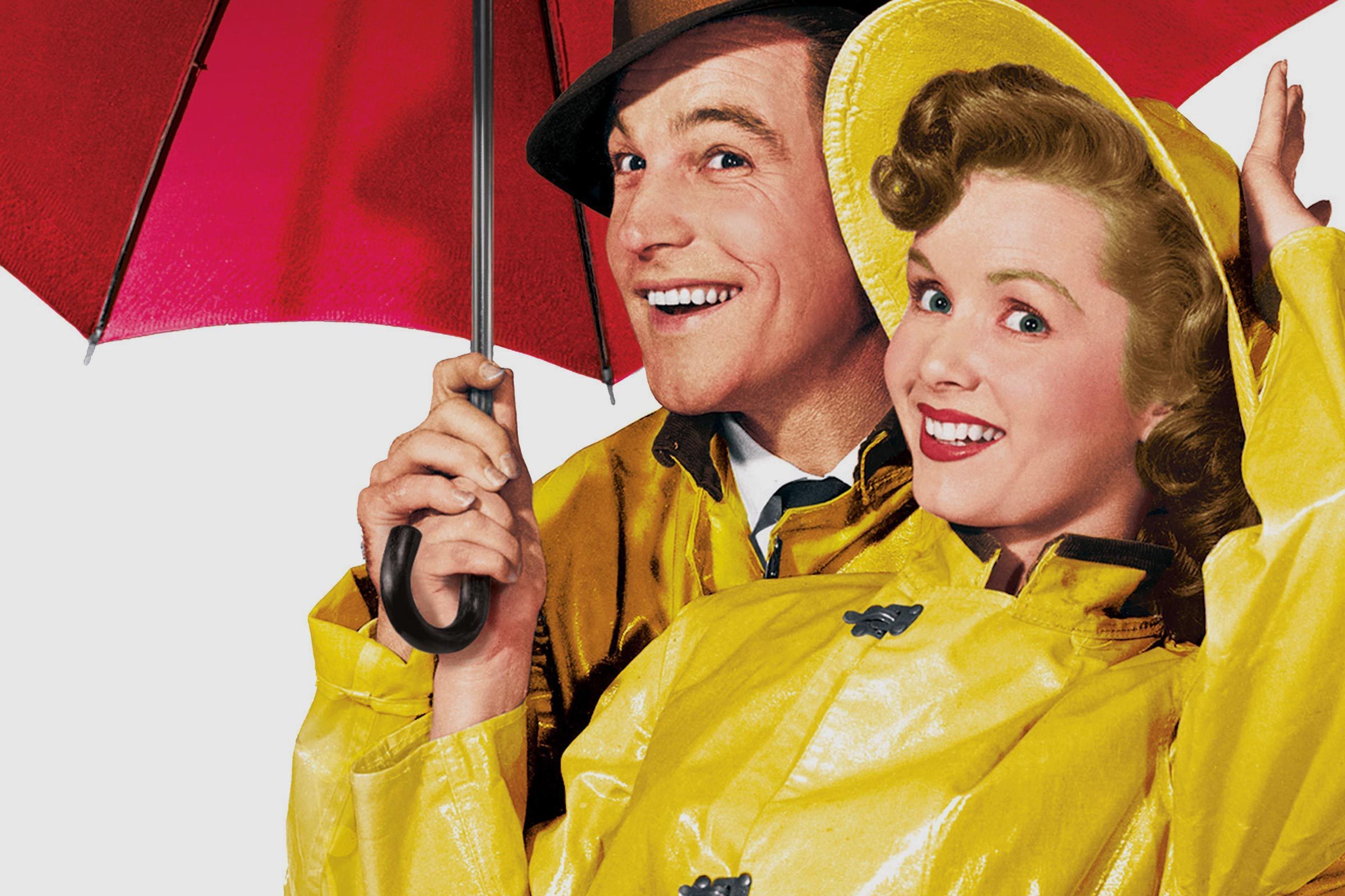 Two people smiling under a red umbrella, wearing bright yellow raincoats, against a plain white background.