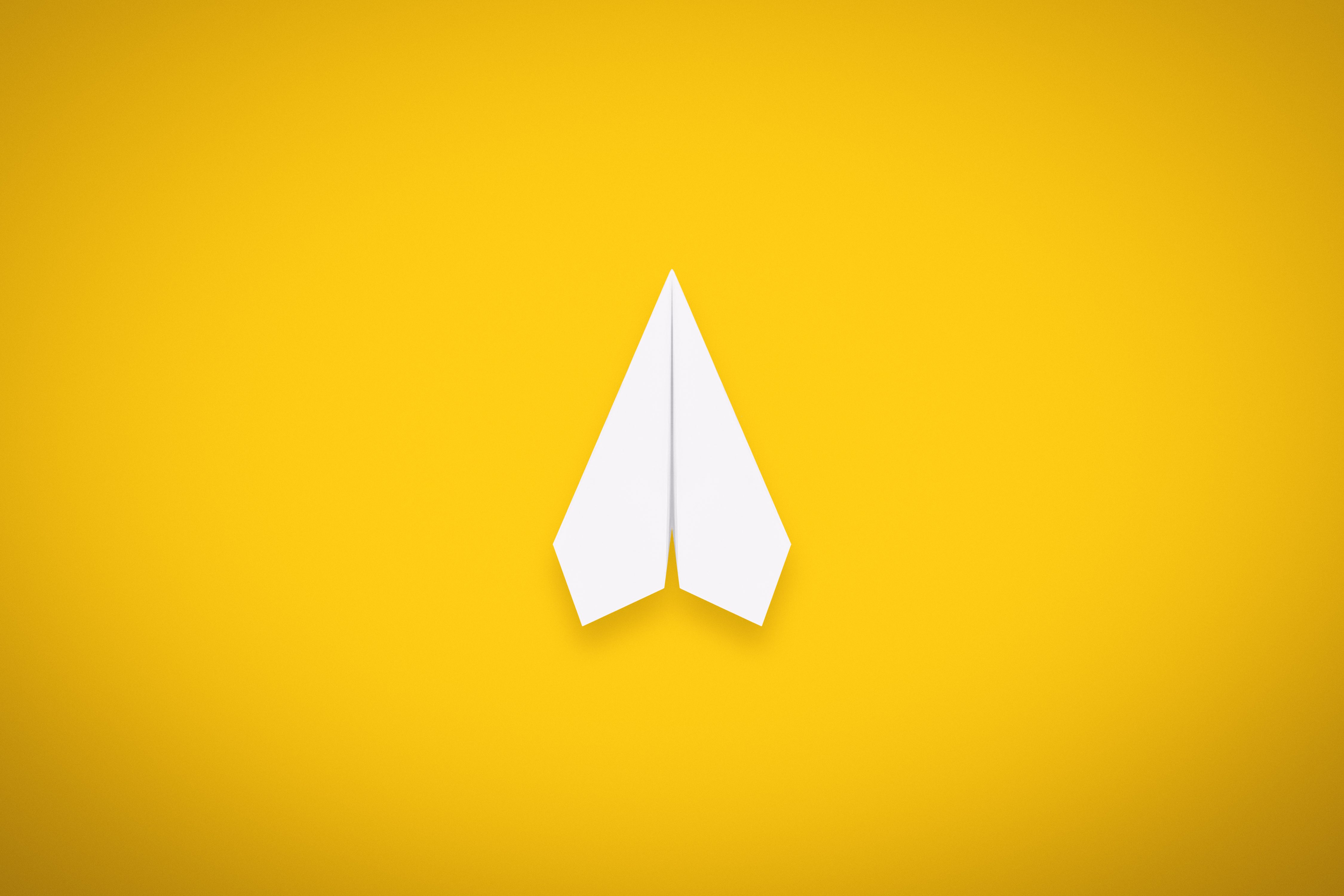 White paper plane stationary on a vibrant yellow background.