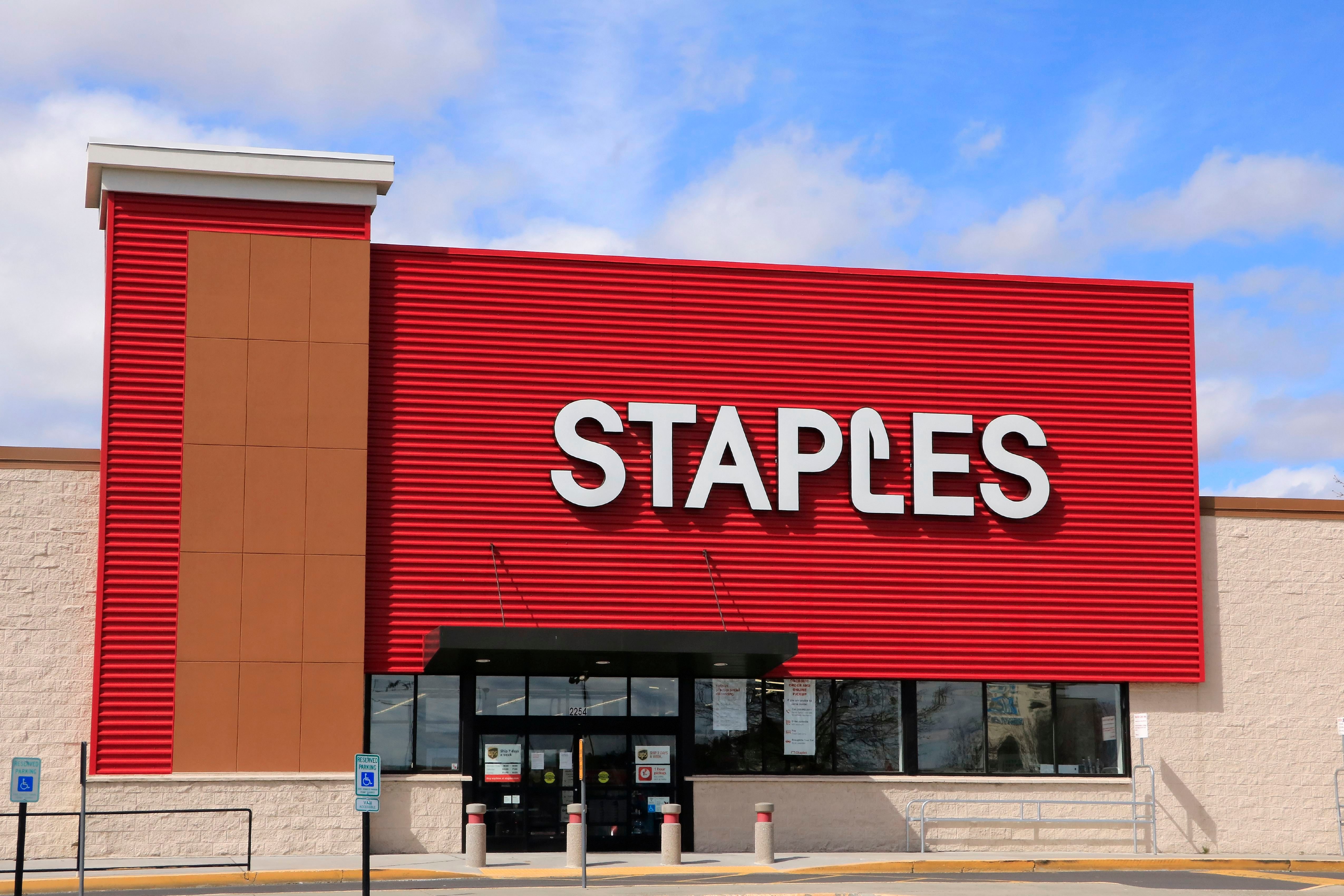 Building displays large "STAPLES" sign, sits under a blue sky with clouds.