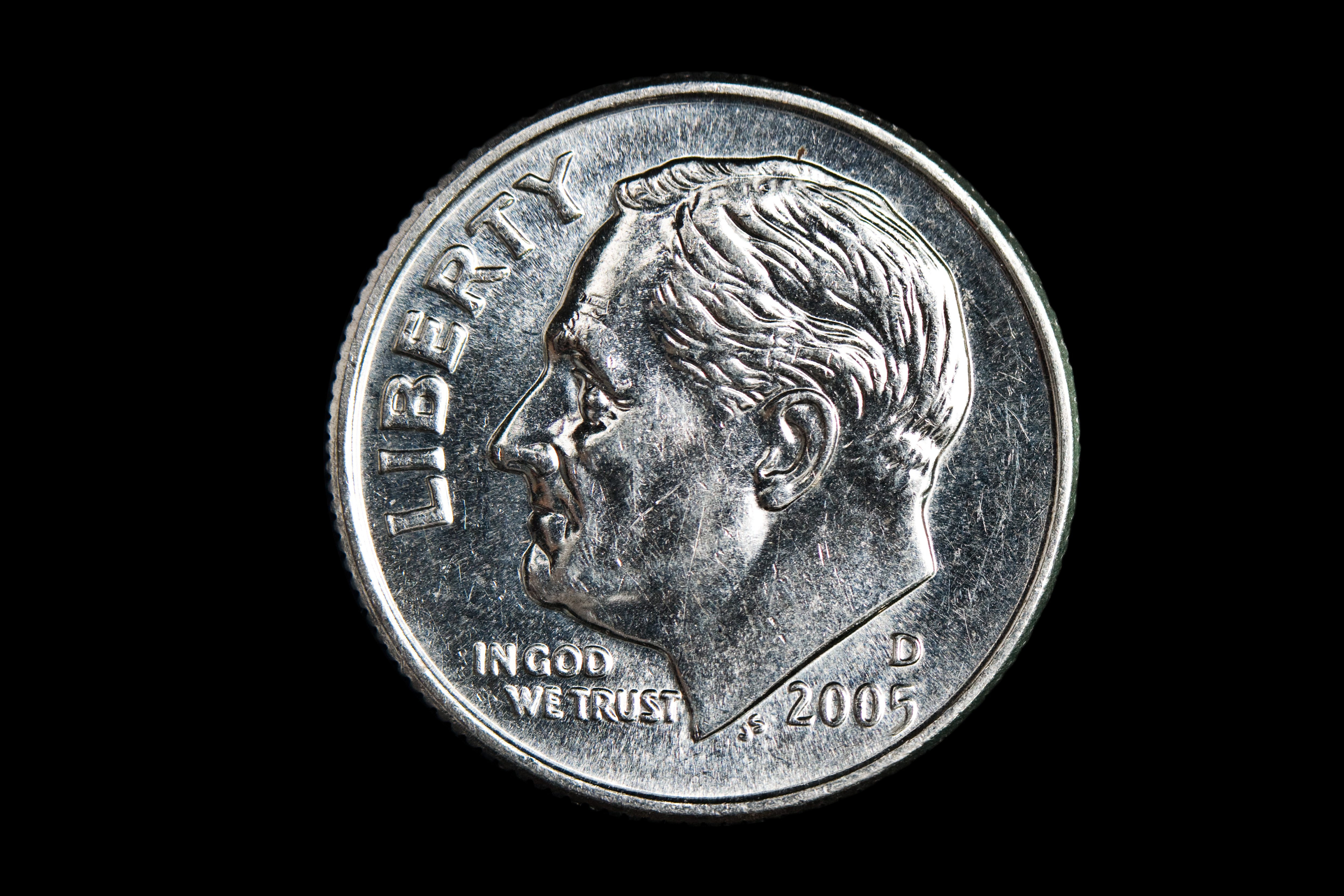 A dime features a profile portrait, inscribed with "LIBERTY," "IN GOD WE TRUST," and the year "2005," against a black background.