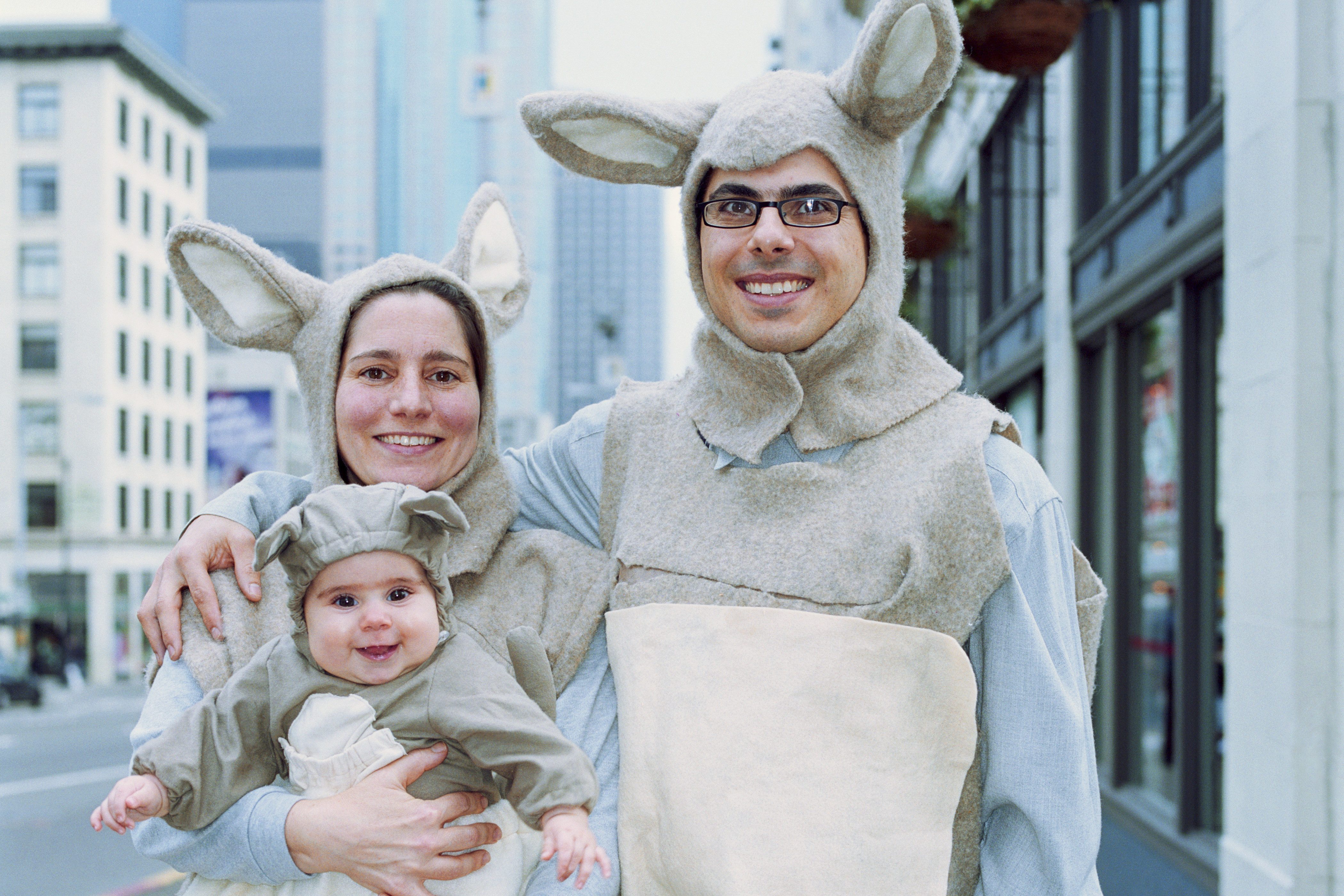 Three people wear kangaroo costumes, smiling in an urban street with buildings.