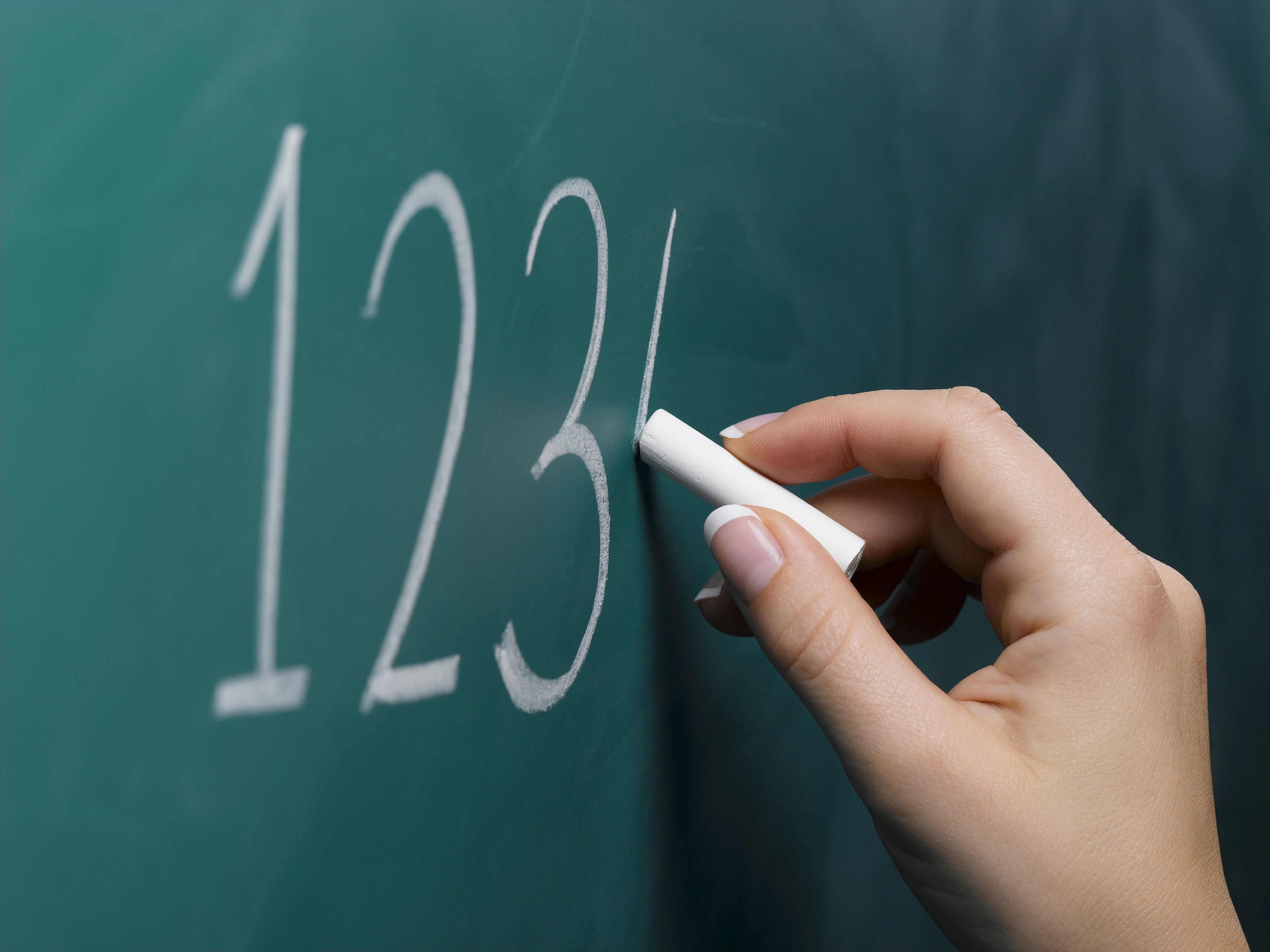 Hand writing "123" with chalk on a green chalkboard.