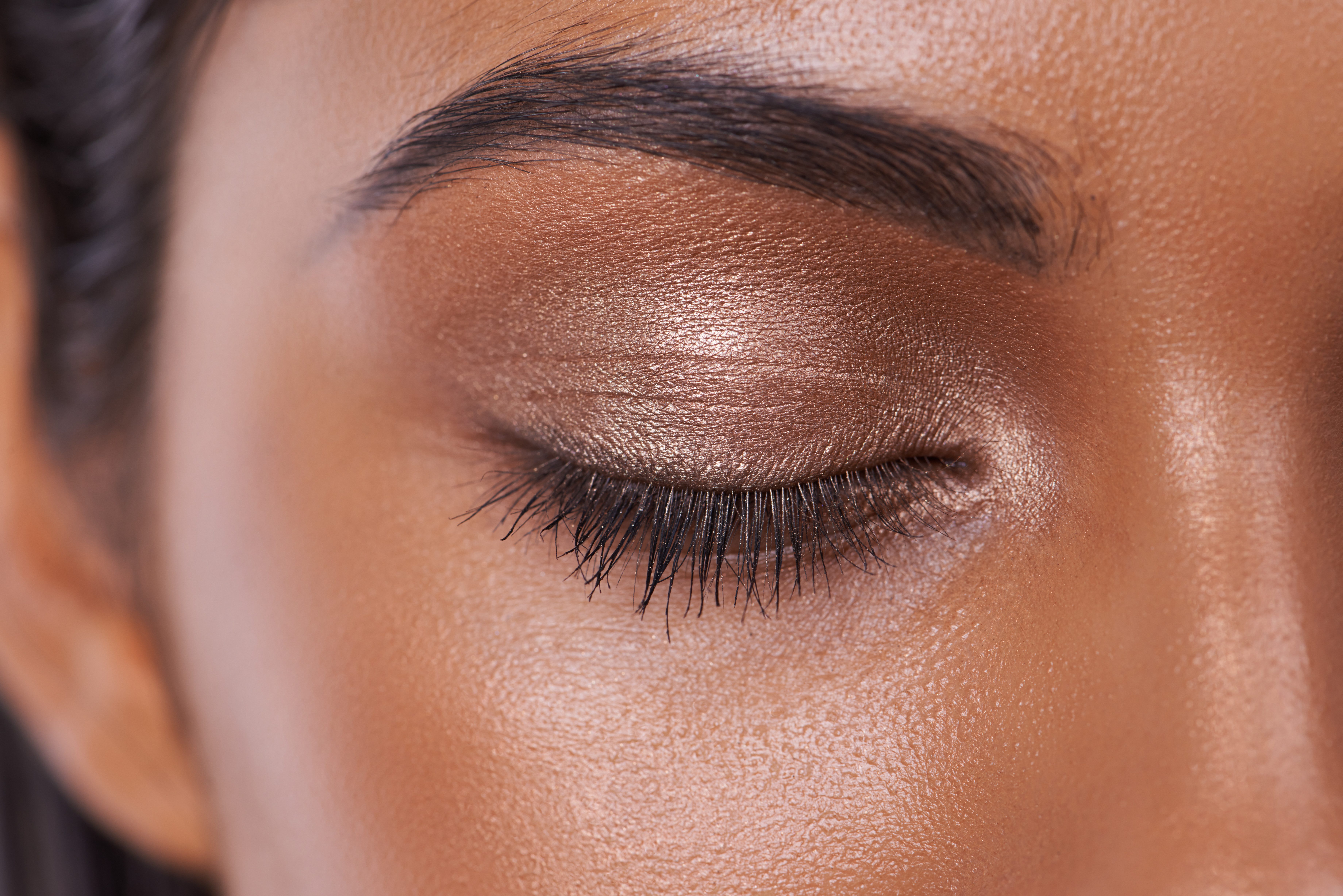 Eyelid closed with shimmering bronze eyeshadow, surrounded by smooth skin.