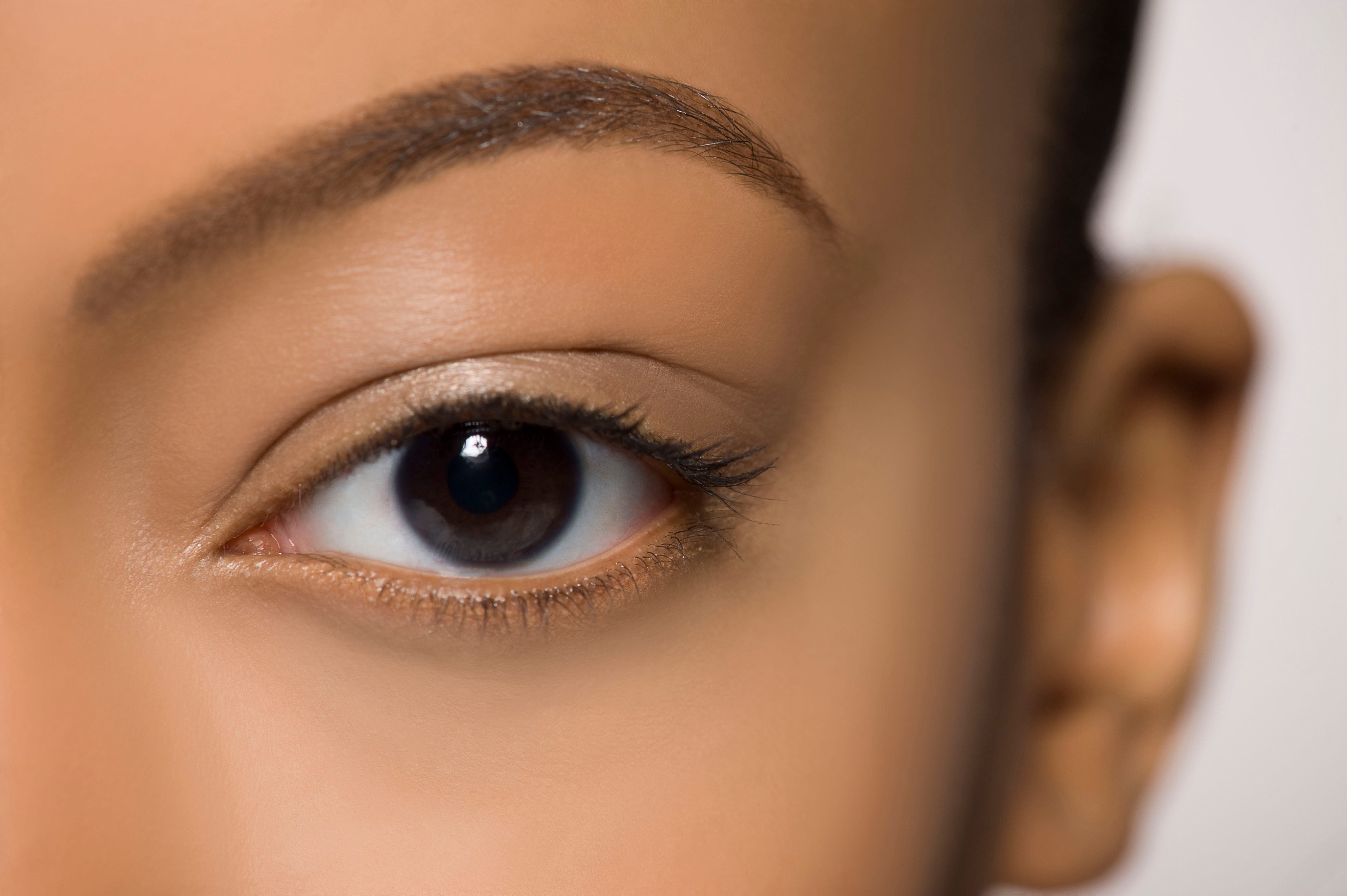 An eye gazes forward, framed by well-defined eyebrow and smooth skin, set against a soft, neutral background.