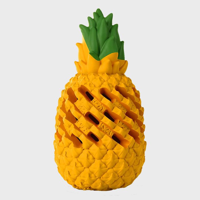 A rubber pineapple toy features textured yellow surface and green leaves, with diagonal cutouts revealing an internal cavity, set against a plain white background.
