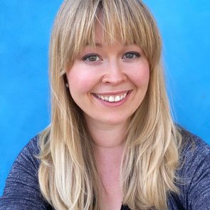 Person smiling against a bright blue background, wearing a black top and a dark cardigan.