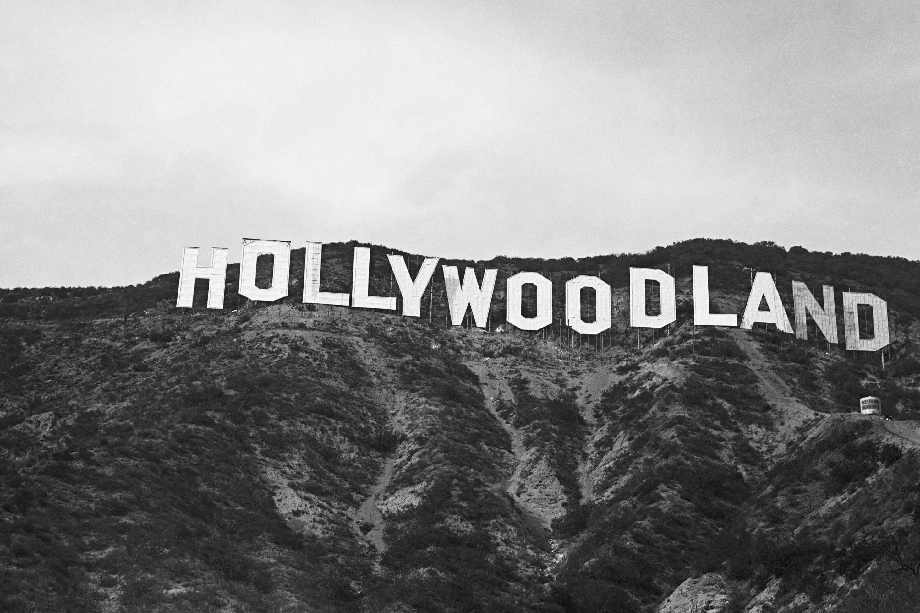 White letters form "HOLLYWOODLAND," standing across a hilltop, surrounded by rugged terrain and sparse vegetation under a cloudy sky.