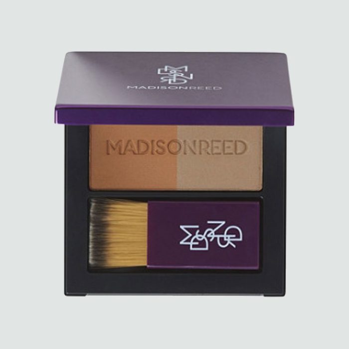 Makeup compact displays dual-tone powders, features embedded brush, on branded purple case with 