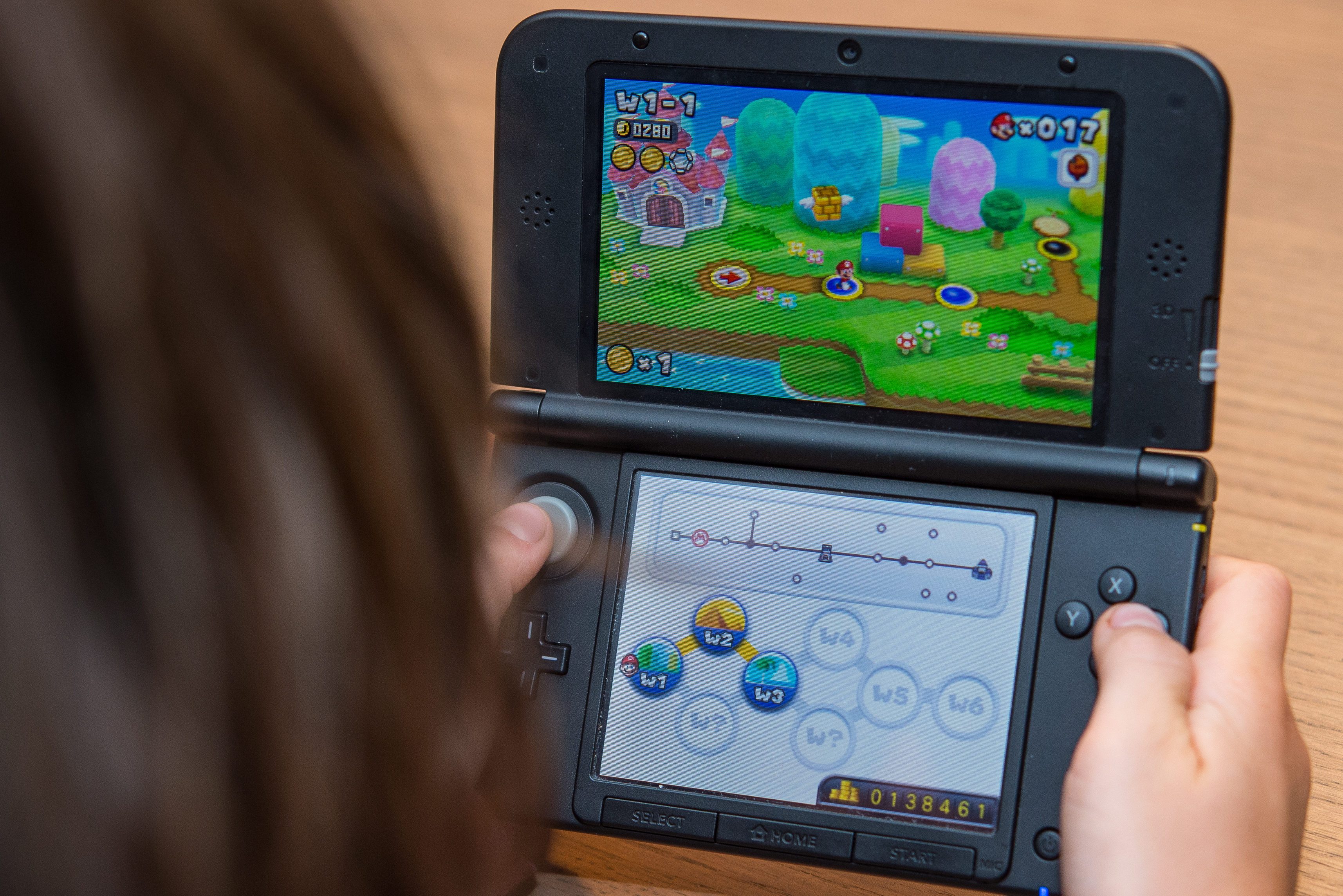 A person plays a handheld gaming console, showing a colorful video game with paths and coins on the screen.