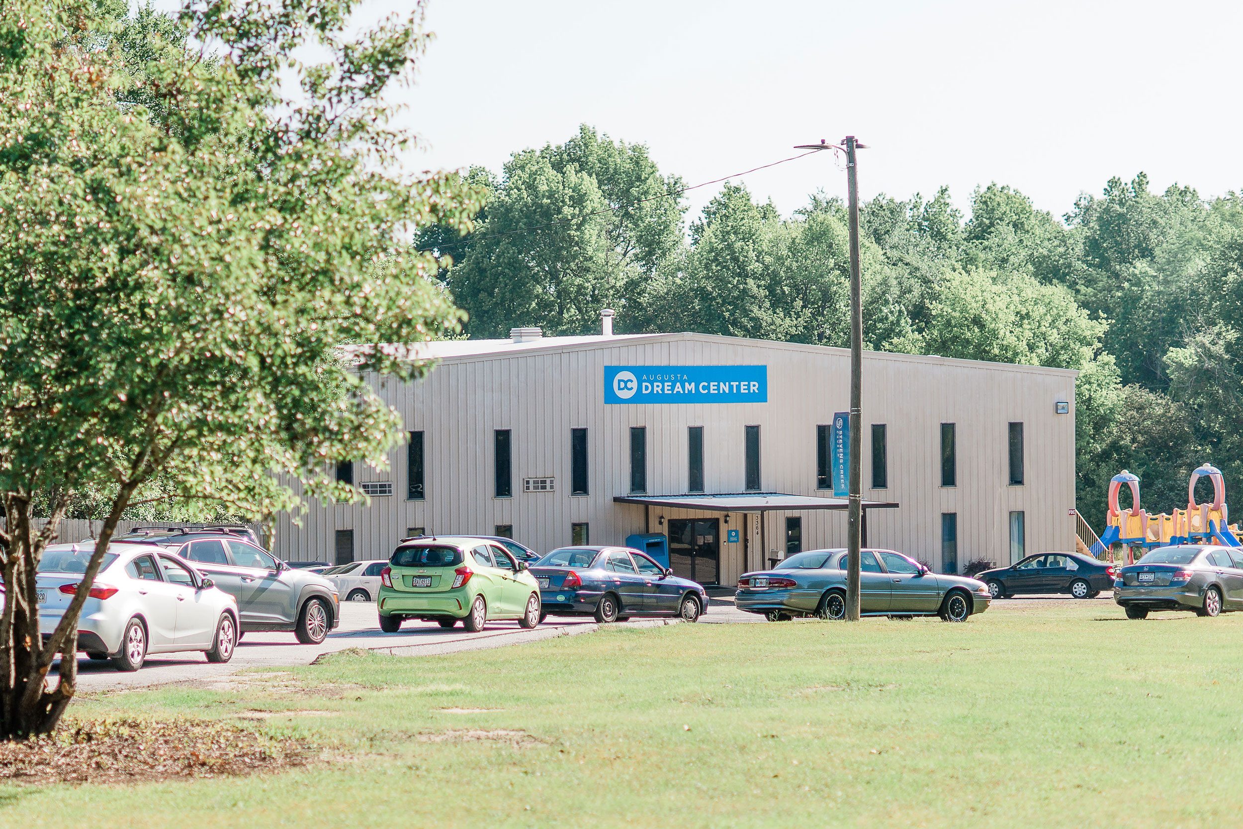 Building displays "Augusta Dream Center" sign, surrounded by parked cars, set in a grassy area with trees.