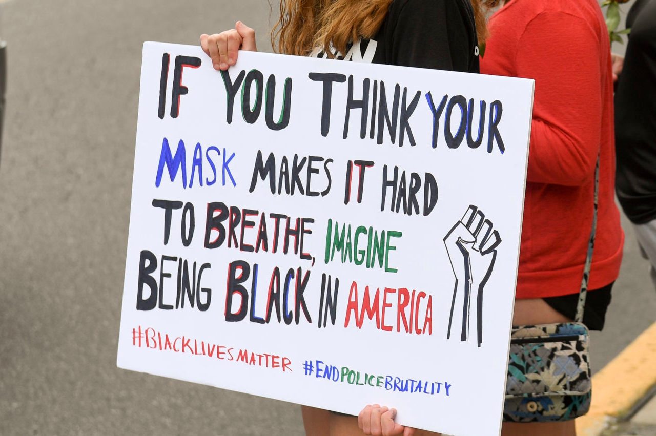 A person holds a protest sign reading, â€œIf you think your mask makes it hard to breathe, imagine being Black in America.â€
