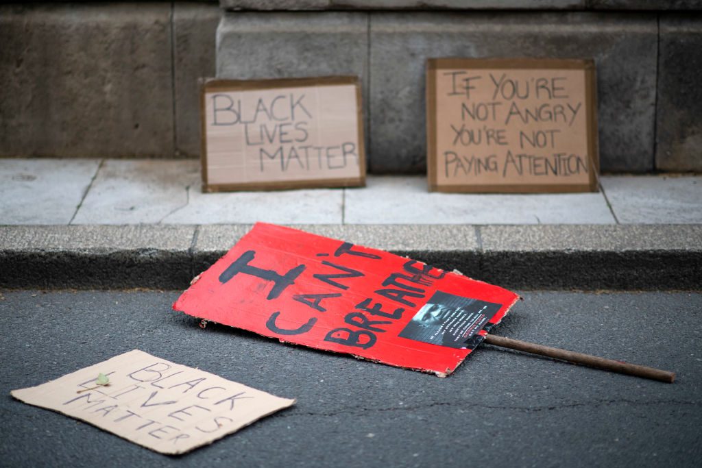 Signs lie on pavement; one reads "I CAN'T BREATHE," another "BLACK LIVES MATTER," and a third states "IF YOU'RE NOT ANGRY YOU'RE NOT PAYING ATTENTION."
