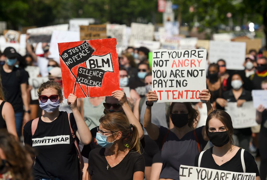 Protesters hold signs reading "No Justice No Peace BLM Silence is Violence" and "If you are not angry you are not paying attention," in a demonstration.