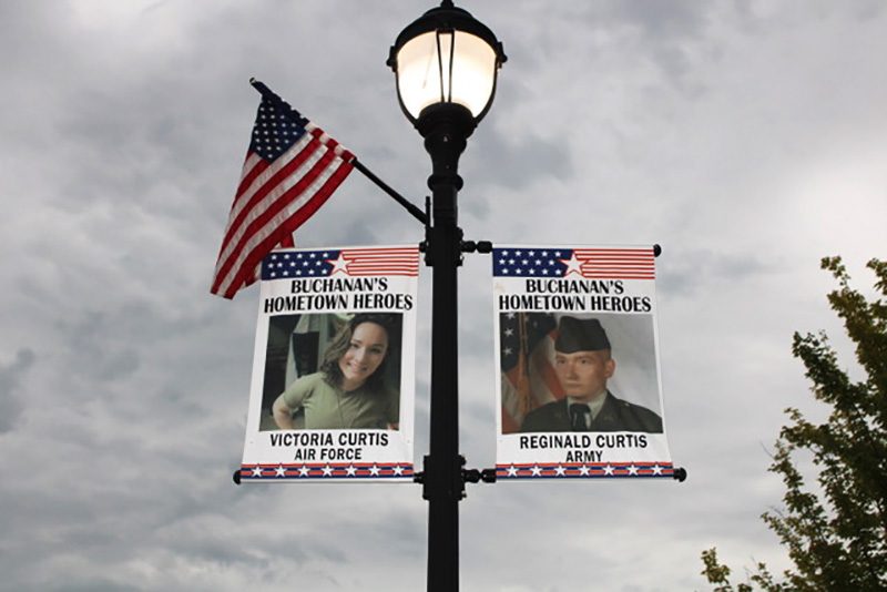 Street banners honor military personnel; one features Victoria Curtis, Air Force, the other Reginald Curtis, Army. An American flag adorns the lamppost above.