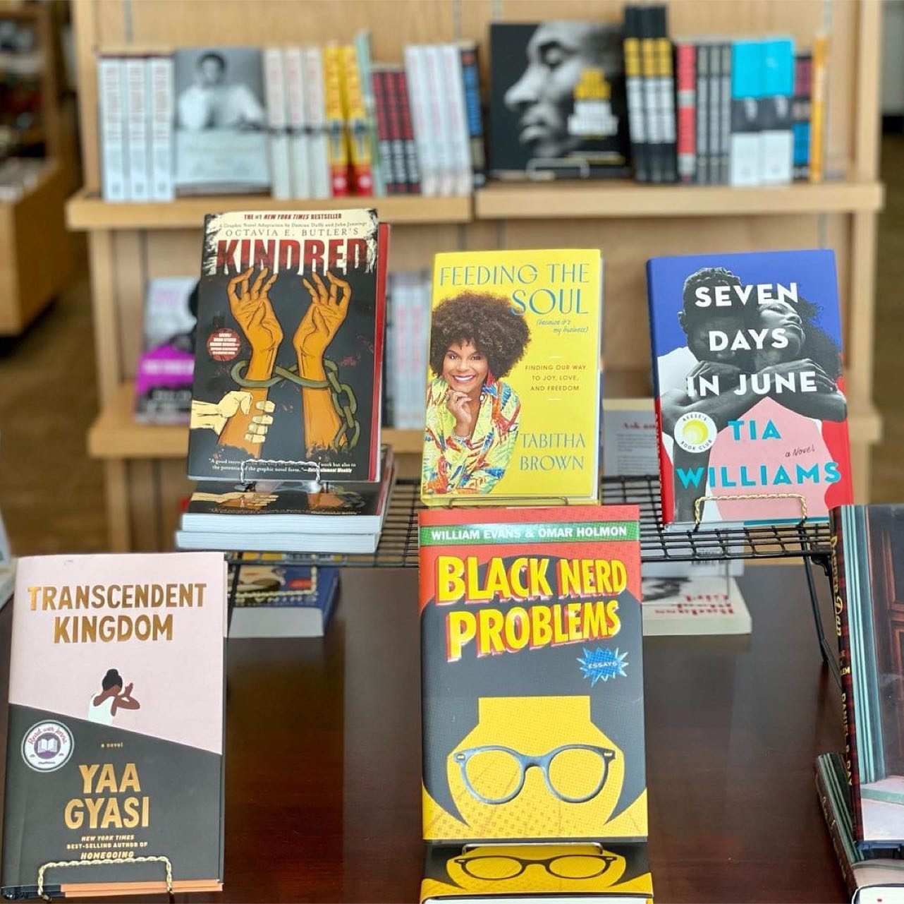 Books are displayed standing upright on a table in a bookstore. Titles include "Kindred," "Feeding the Soul," "Seven Days in June," "Transcendent Kingdom," and "Black Nerd Problems."