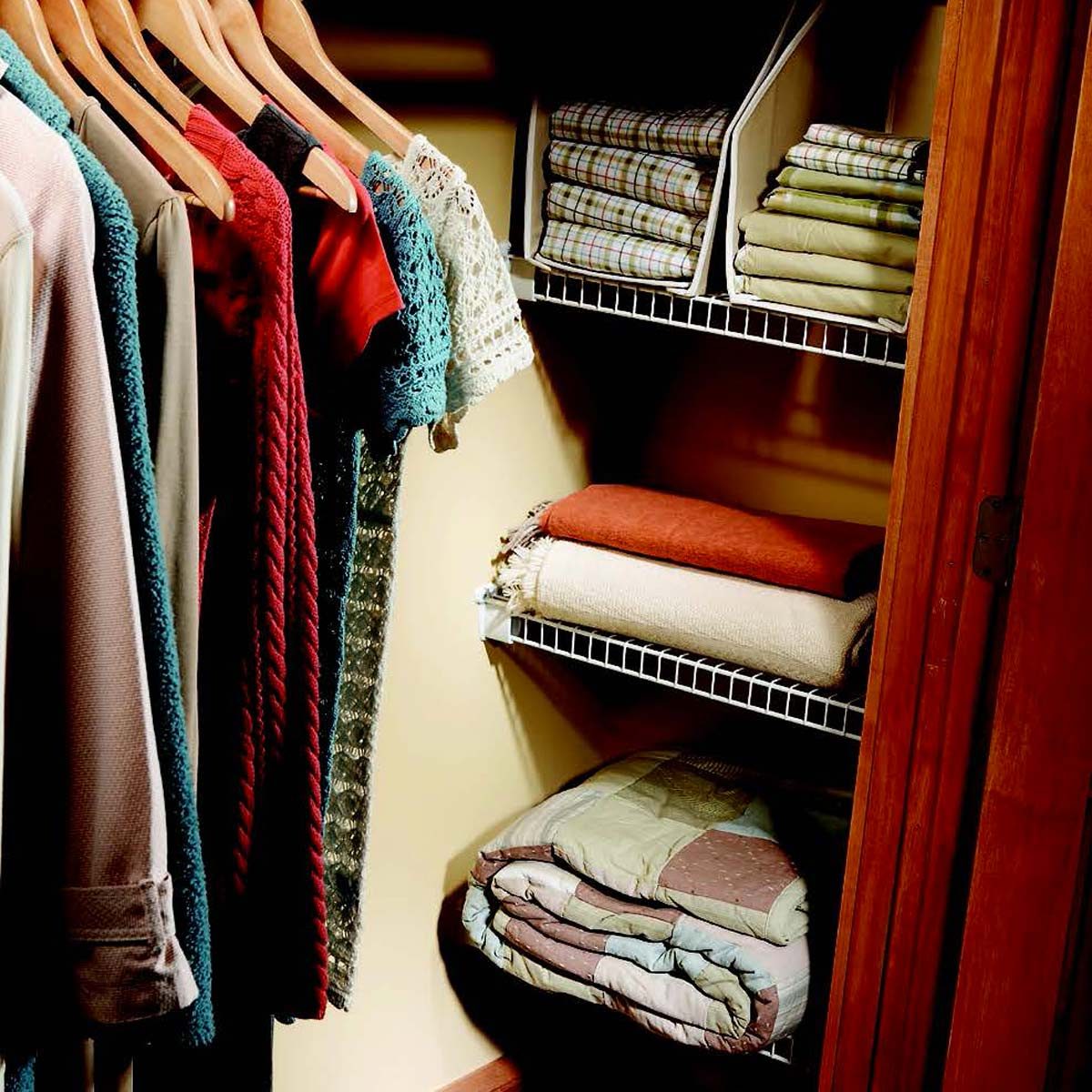 Clothes hang neatly on wooden hangers, shelves hold stacked blankets and folded linens, within a small closet space.